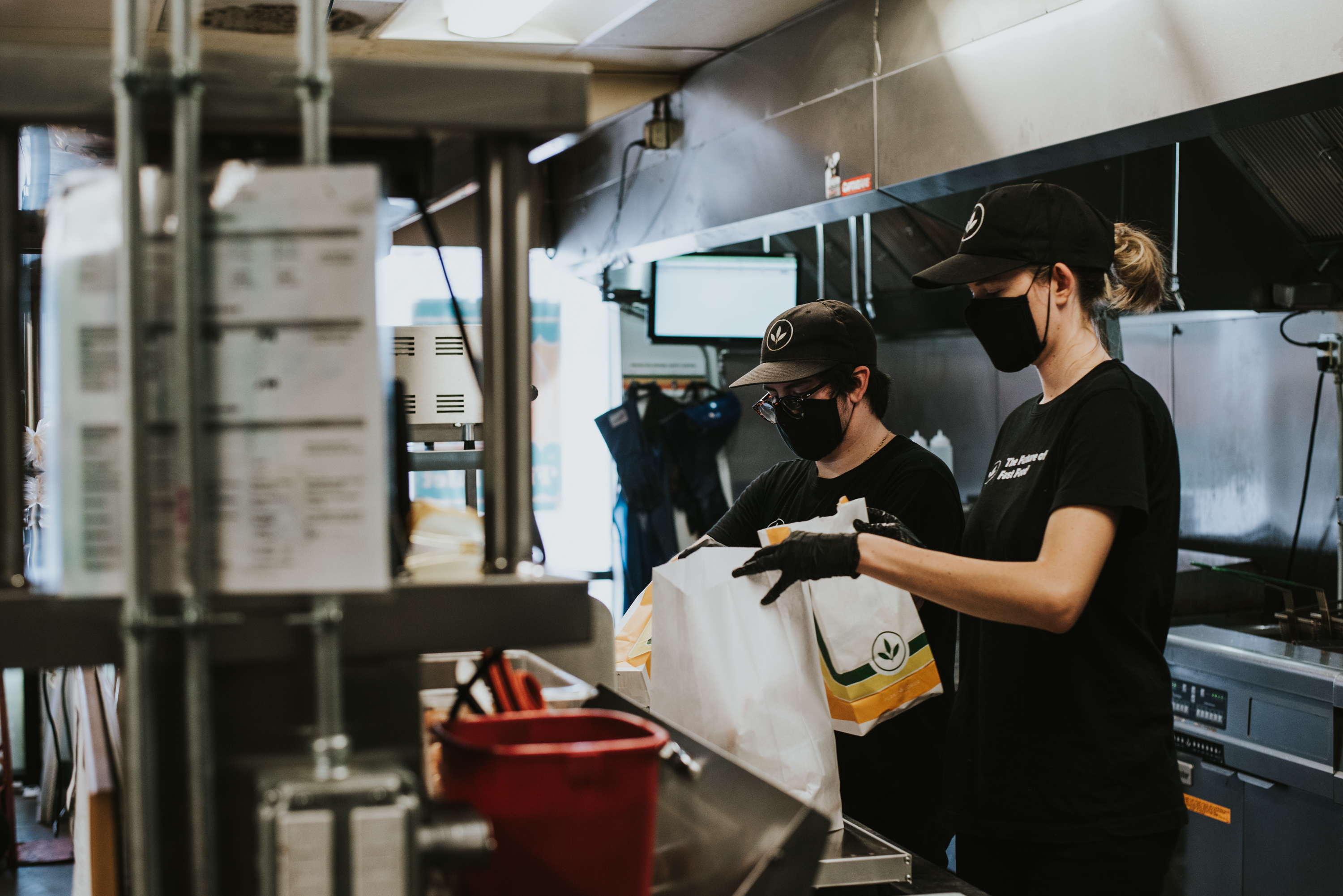 two kitchen workers in masks prepare takeout food for plant power fast food